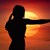 Silhouette einer Frau steht mit ausgestrecktem Arm vor gelber Sonne